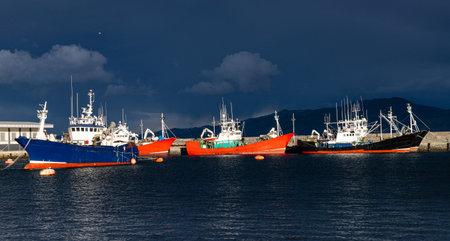 Colorful fishing boats anchored at the harbor with a dramatic stormy sky in the background, capturing a serene maritime scene.の写真素材