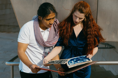 Intently focused, two professionals review an art portfolio, collaborating in an outdoor urban setting.の写真素材