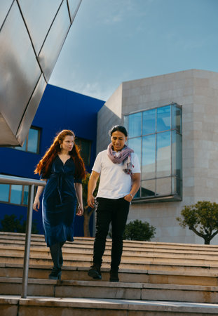 Two friends walk down the stairs of a modern urban building, enjoying a leisurely day out in the...