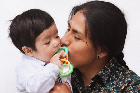 An Ecuadorian father with a traditional braid gently kisses his baby, symbolizing love and cultural...