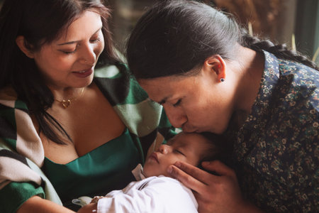 The mother looks on affectionately while the gently kisses the child, exemplifying the deep...