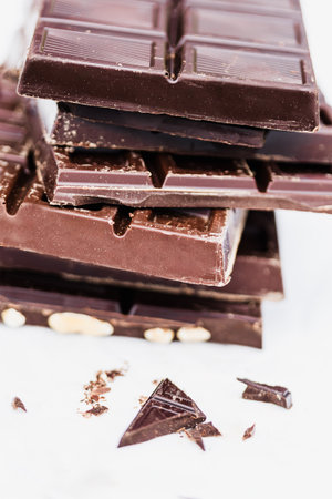 A stack of various chocolate bars with broken pieces on a white background. Perfect for dessert and...