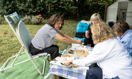 A group of women friends sharing a meal at an outdoor picnic in the countryside, enjoying food and...