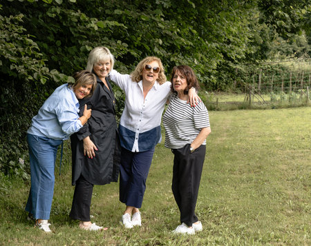 Four mature friends enjoying a picnic in the countryside, standing together and smiling in a lush...