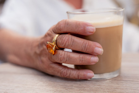 A close-up of a woman's hand holding a coffee glass, wearing a large ring.