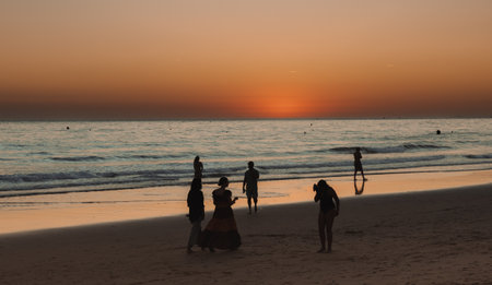 Group of people enjoying a walk on the beach during sunset