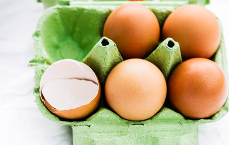 Close-up of a green egg carton holding four brown eggs and an empty eggshell.