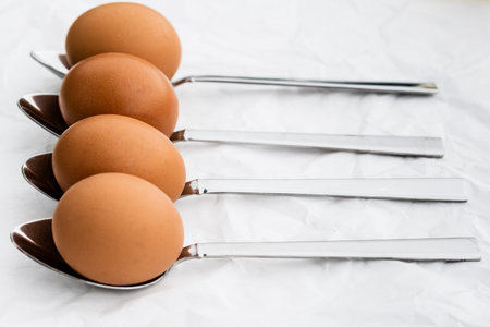 Close-up of four brown eggs arranged on stainless steel spoons on a white background.の写真素材