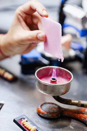 A person is holding a pink object over a flame. The object is likely a wax or plastic material, and...