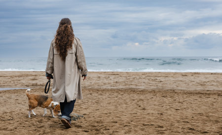 Woman and beagle strolling on the beach under a cloudy sky by the oceanの写真素材