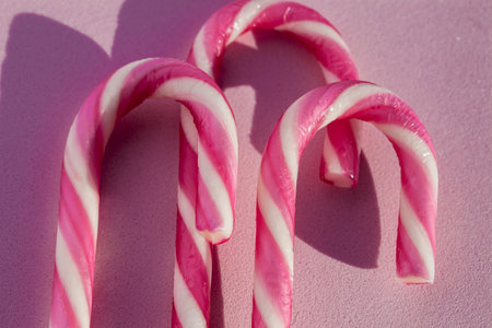 Close-up of festive pink and white candy canes on a soft pink surface with shadows.