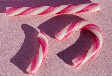 A broken pink and white candy cane placed in a creative arrangement on a pastel pink surface.