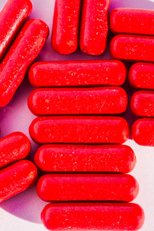 Close-up of red candies arranged on a pink background with soft shadows.の写真素材