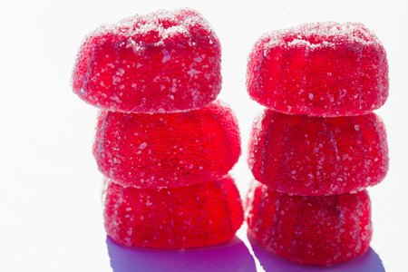 Close-up of stacked red gummies covered in sugar crystals on a white surface.