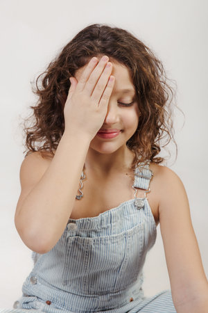 Casual girl sitting in studio, playfully covering one eye with her handの写真素材
