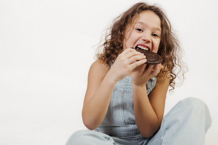 Happy 8-year-old girl enjoying a chocolate snack indoors with a joyful expressionの写真素材