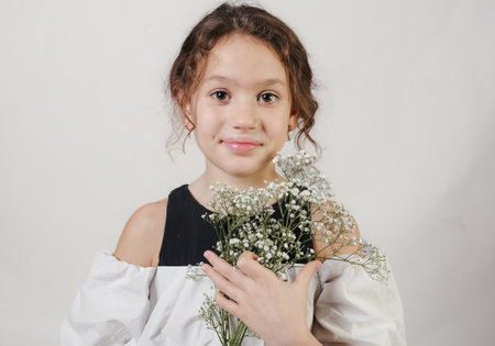 Smiling young girl in a studio holding a bouquet of flowers and looking at the cameraの写真素材