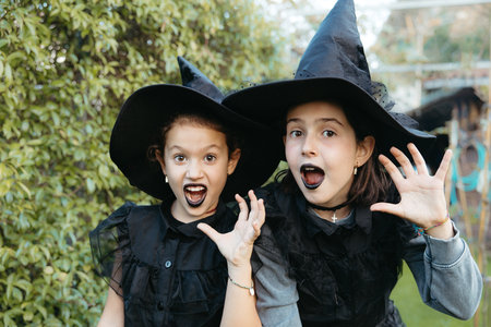 Two young girls dressed as witches making expressions while playing outdoors in a garden.