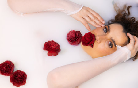 Artistic portrait of woman in milk bath with red camellias