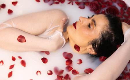 Elegant woman in milky bath with red petals on her skin