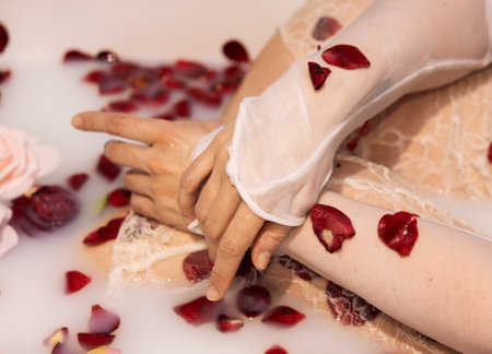 Detail of woman's arms in milk bath with lace and flower petalsの写真素材