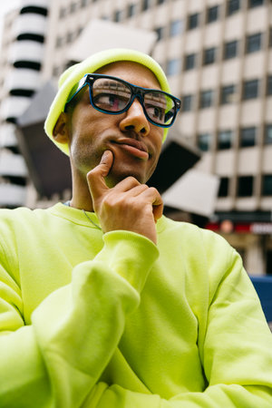 Pensive multiracial man in glasses and neon clothes on city streetの写真素材