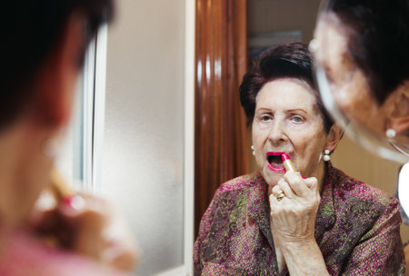 Elderly woman putting on makeup at home with mirror reflectionの写真素材