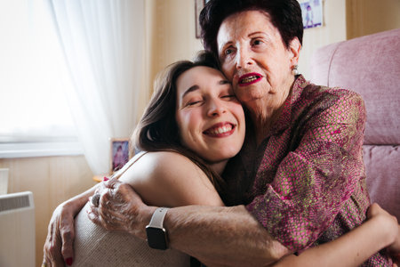 Touching moment of a young woman embracing her elderly grandmother in the living roomの写真素材