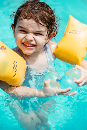 Three-year-old girl smiling with floaties in a backyard poolの写真素材