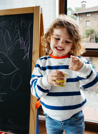 Smiling toddler girl enjoying yogurt snack indoors