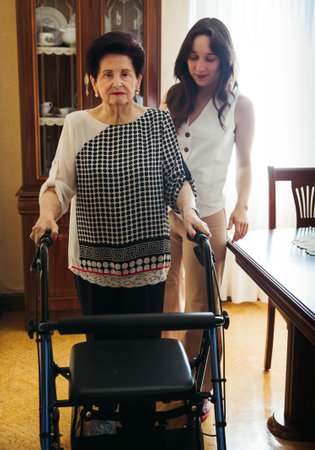Young woman helping elderly grandmother walk with a walker at homeの写真素材