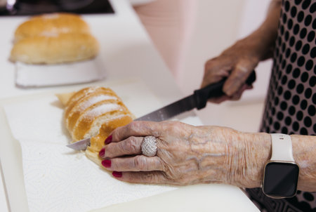 Close-up of elderly woman slicing sweet bread at home kitchenの写真素材