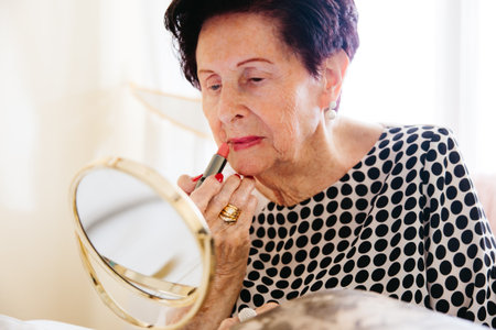 Senior woman putting on lipstick in front of a mirror at home