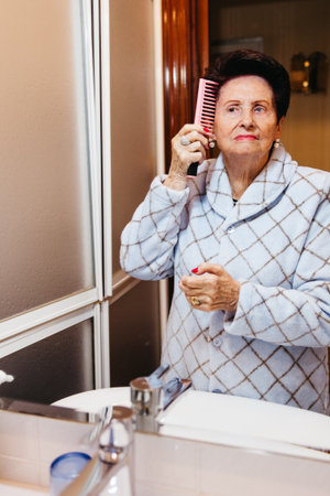 Senior woman brushing hair while looking in the bathroom mirrorの写真素材