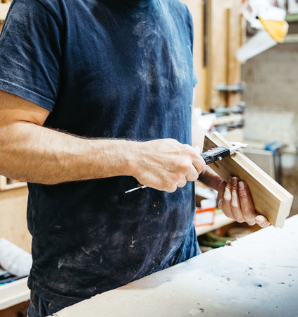 Detail of manual wood measurement using caliper in woodworking workshop