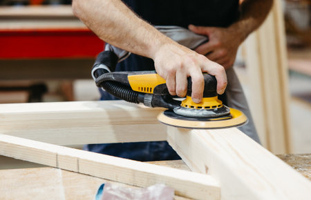 Hands sanding wood with a power sander in a professional workshopの写真素材