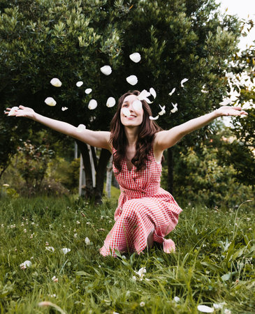 Young woman smiling and throwing petals in the air in a gardenの写真素材