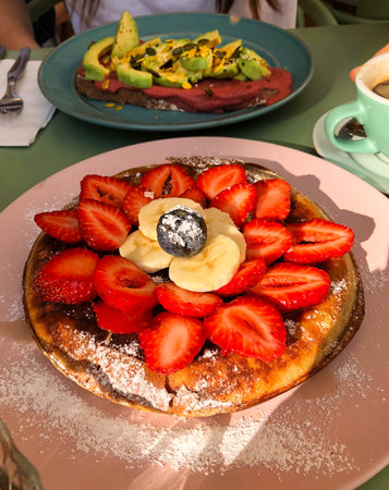 Pancakes with berries and toast with avocado and salmon on terrace