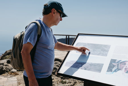 Man exploring cultural information panel in natural viewpoint on sunny dayの写真素材