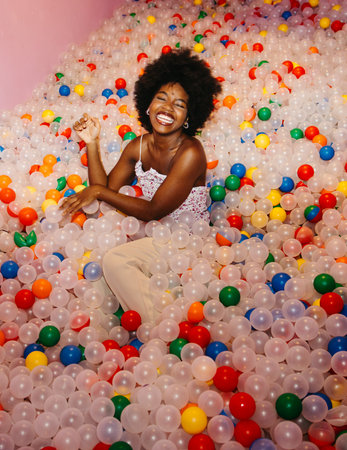 Vertical shot of a smiling young woman sitting in a vibrant ball pool.の写真素材