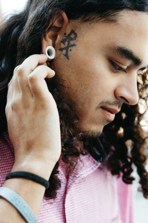 Profile portrait of a young man with tattooed temple, curly hair and ear plug