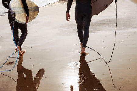 Back view of surfers walking with boards on wet sand at sunsetの写真素材