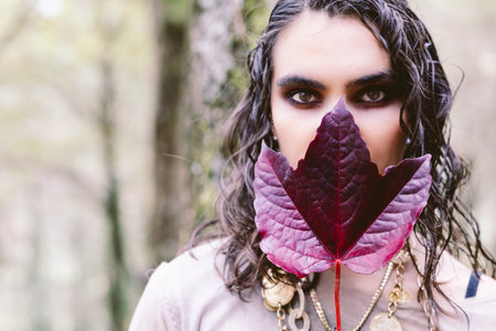 Portrait of a woman hiding her lips with a red autumn leaf in the forestの写真素材