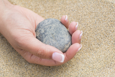 A woman holds a pebble in her hand. In the sand of the beach. Close up.の写真素材