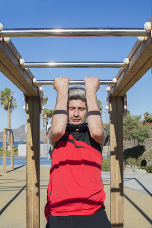 Man practicing sports, calisthenics, in the urban gym outdoors, near the coast, with blue sky and...