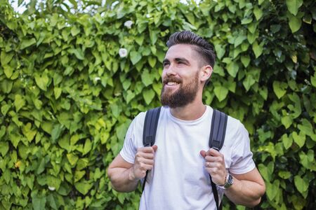 Handsome man smiling with his backpack on a background of green and natural leaves.の写真素材