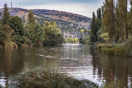 Autumn landscape of a beautiful river with the bridge in the distance, surrounded by trees and vegetation in ocher color by the arrival of autumnの写真素材