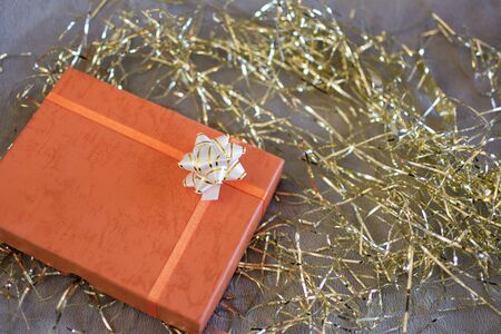 Nice orange gift box with white bow and golden ornaments around.
