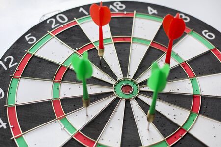 Green and red darts hitting in the dartboard in white backgroundの写真素材
