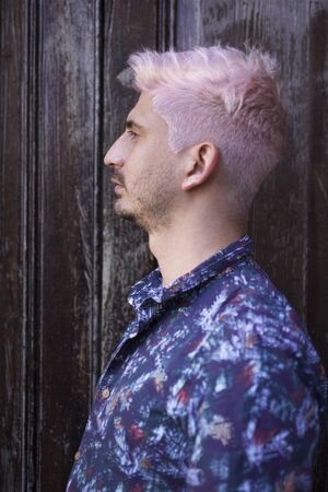 Profile of a young homosexual boy, with pink hair and colored shirt, isolated on old wood texture.